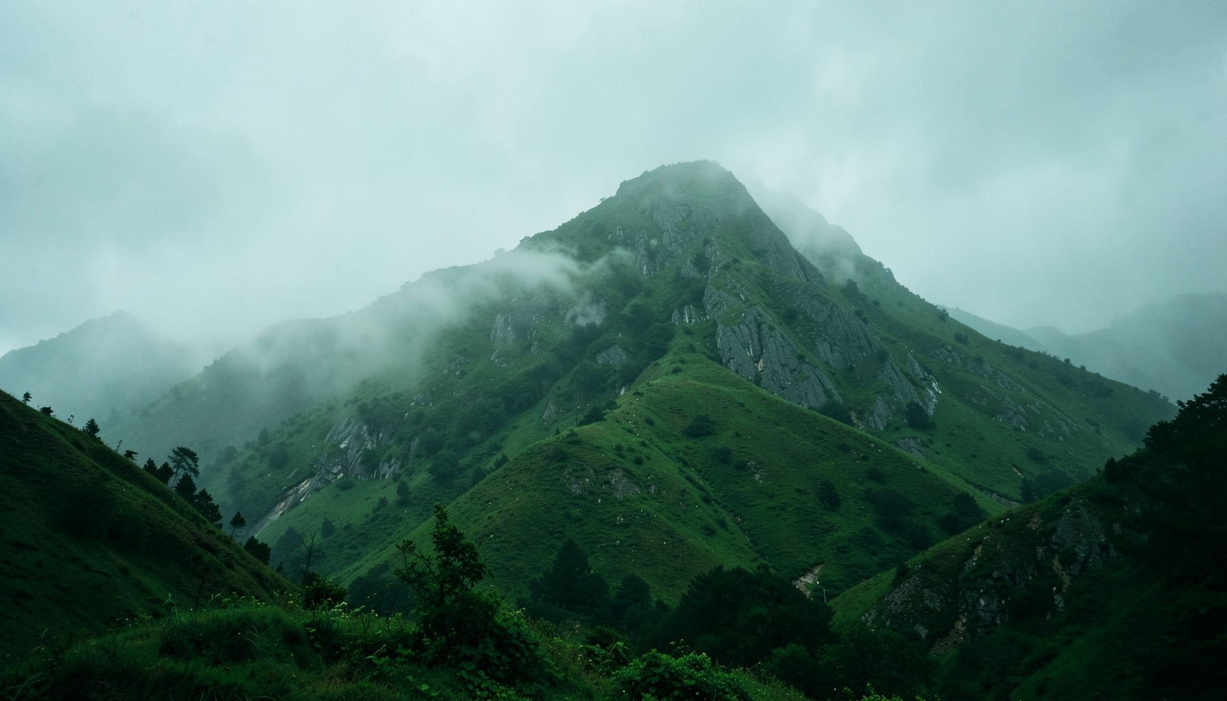 A wide misty green mountain landscape with a rocky peak, moody and atmospheric outdoor scene