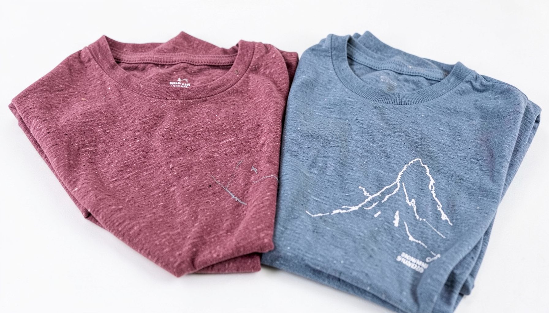 Women's softstyle T-shirts in heather burgundy and slate blue neatly folded with a glimpse of a mountain-inspired graphic
